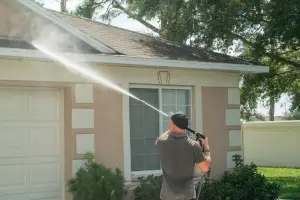 Skilled technician performing roof pressure washing on a residential home to remove dirt, algae, and buildup.