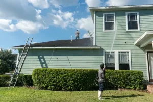 Professional team using roof pressure washing techniques to clean a two-story home.